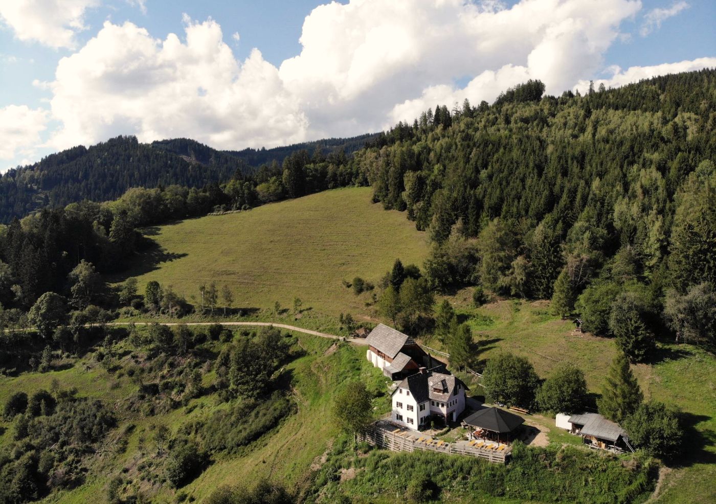 Luftbild: der Hof an der Wiese vor dem Wald, darüber Wolken