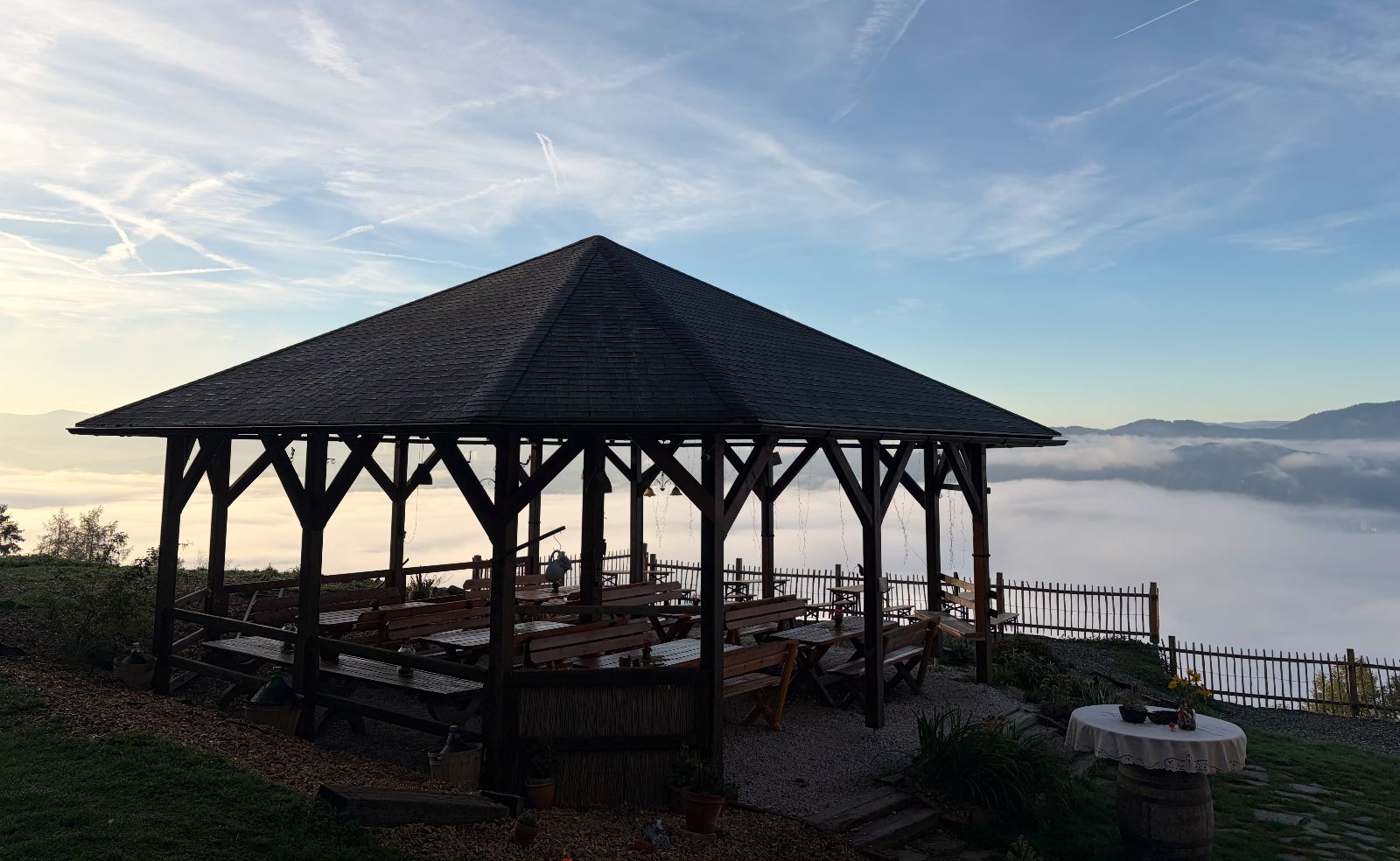 Der Holzpavillon mit Bänken am Morgen, dahinter ein Nebelmeer über dem Tal