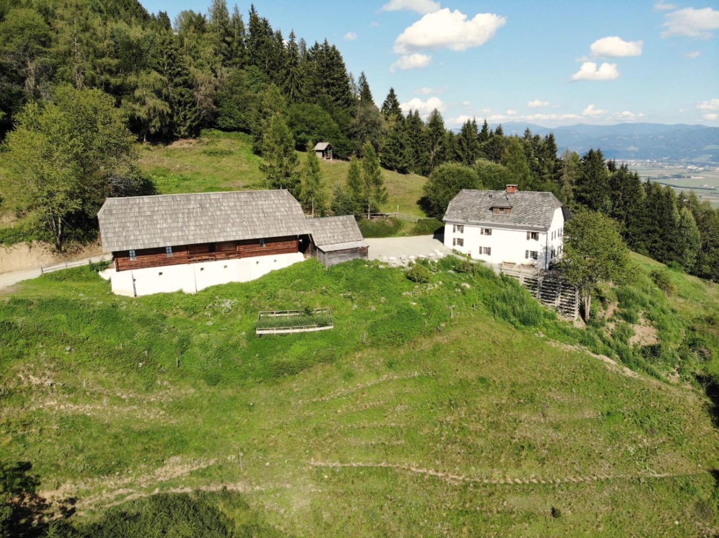 Luftbild: Holzstadl und weißes Wohnhaus auf der Kuppe