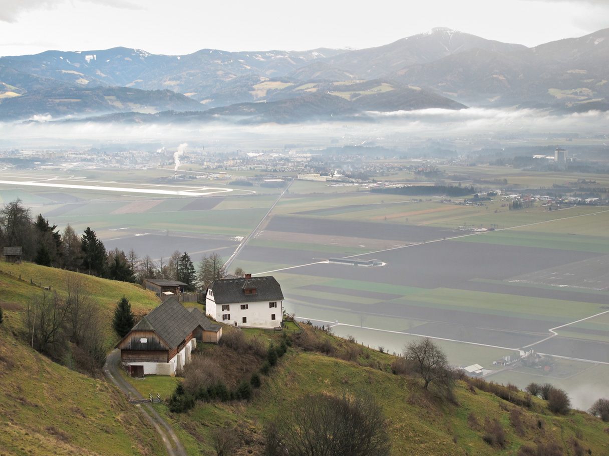 Der Höhn am Hang über dem Aichfeld, Nebel liegt über dem Tal, dahinter die Berge