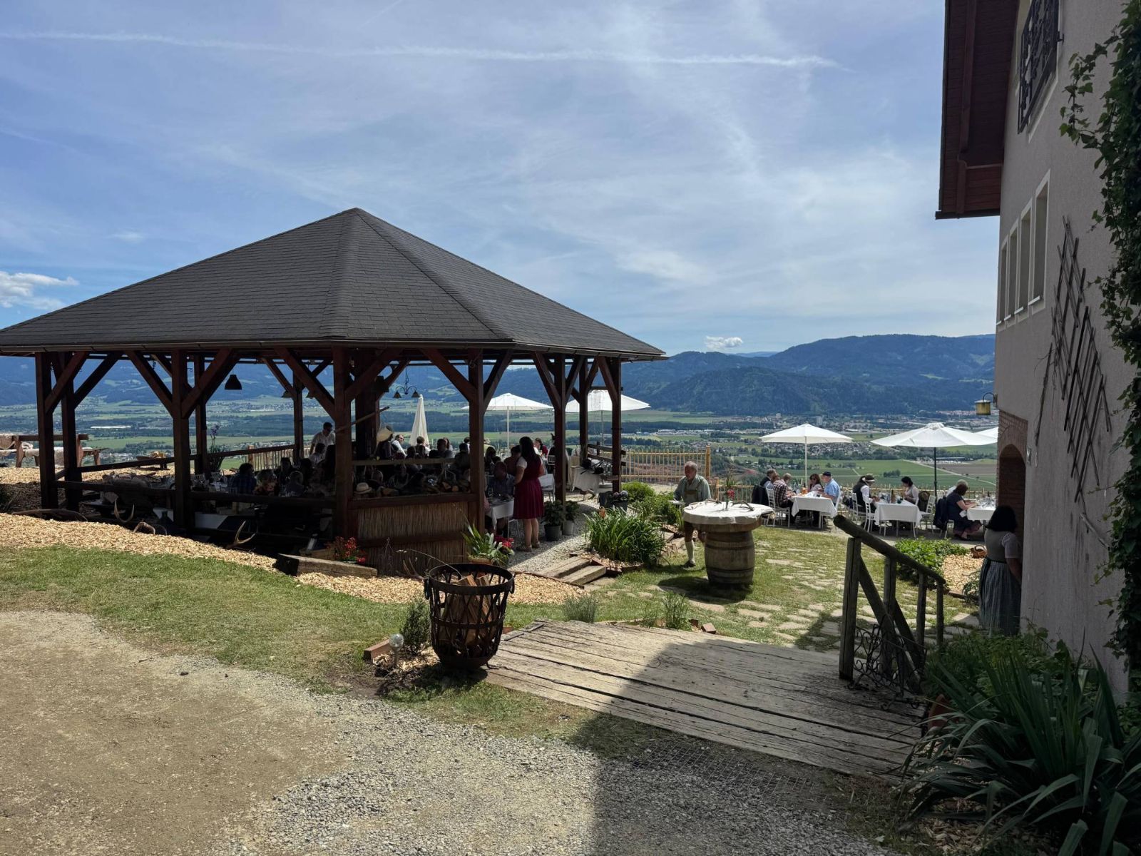 Gäste im Holzpavillon und auf der Terrasse, dahinter das Aichfeld